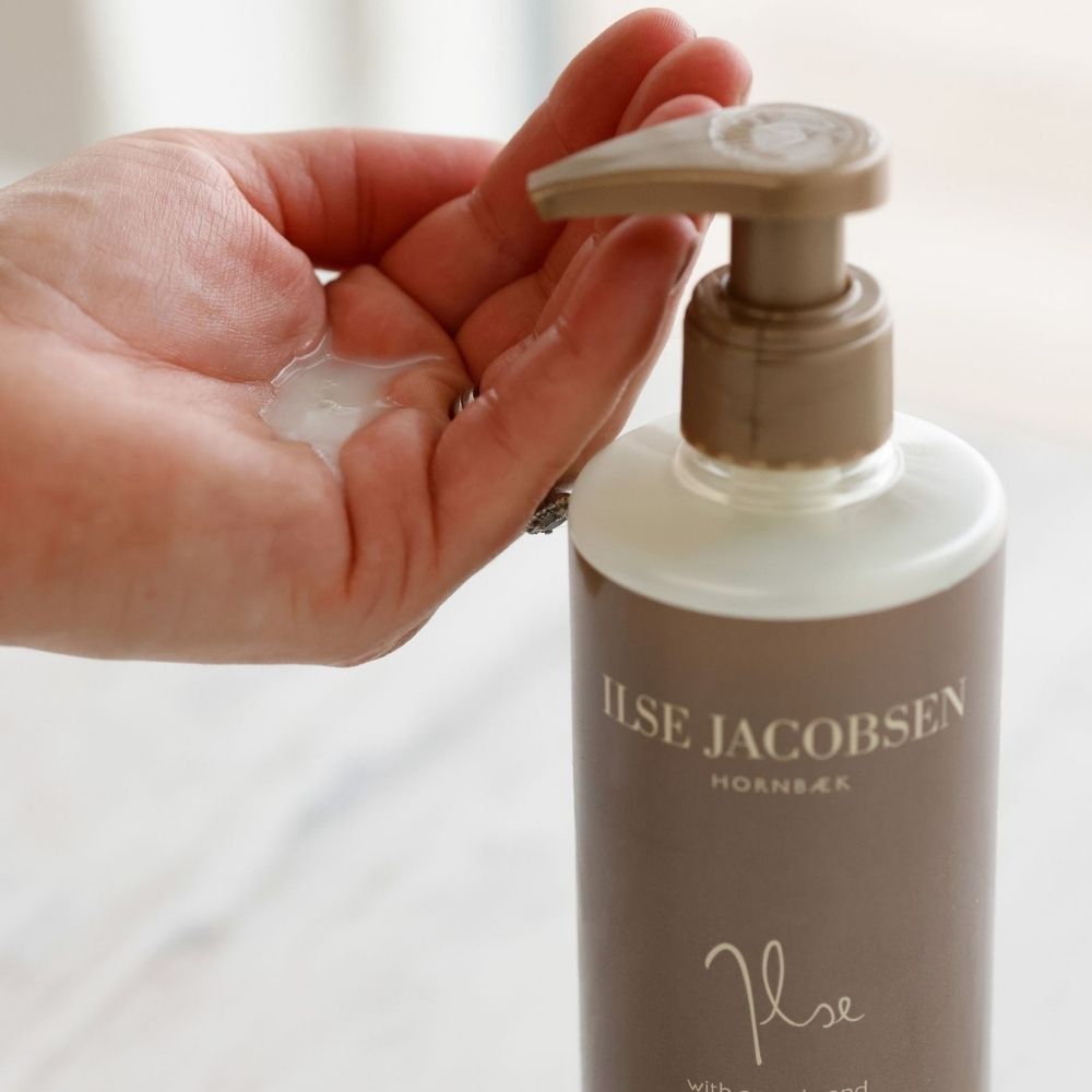 Hand holding a pump bottle of Ilse Jacobsen product with a blurred background