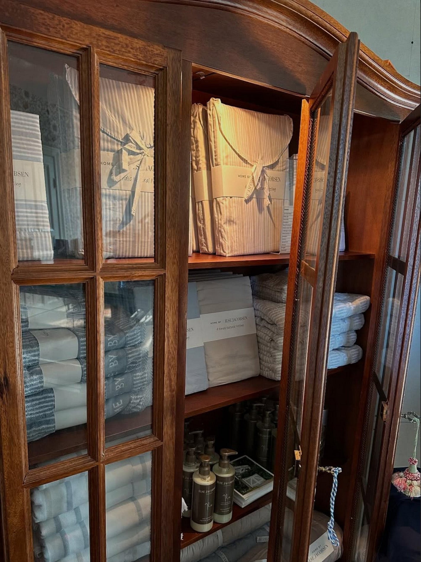 Wooden cabinet with glass doors displaying folded clothes and boxes.